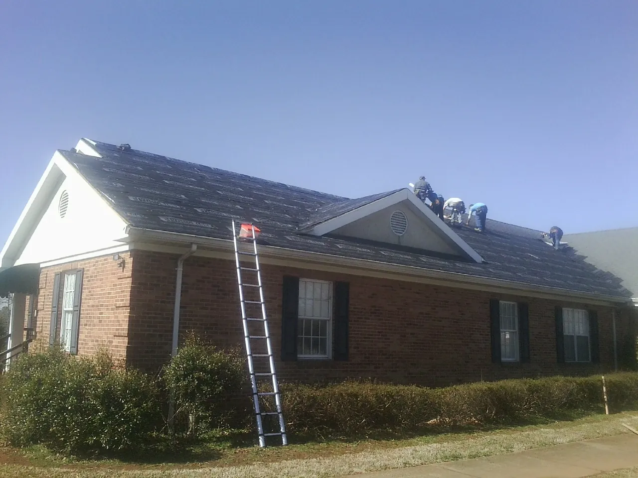 Crew tearing shingles off a brick ranch roof with a ladder set — Emergency Roof Repair work by our crew in Caldwell