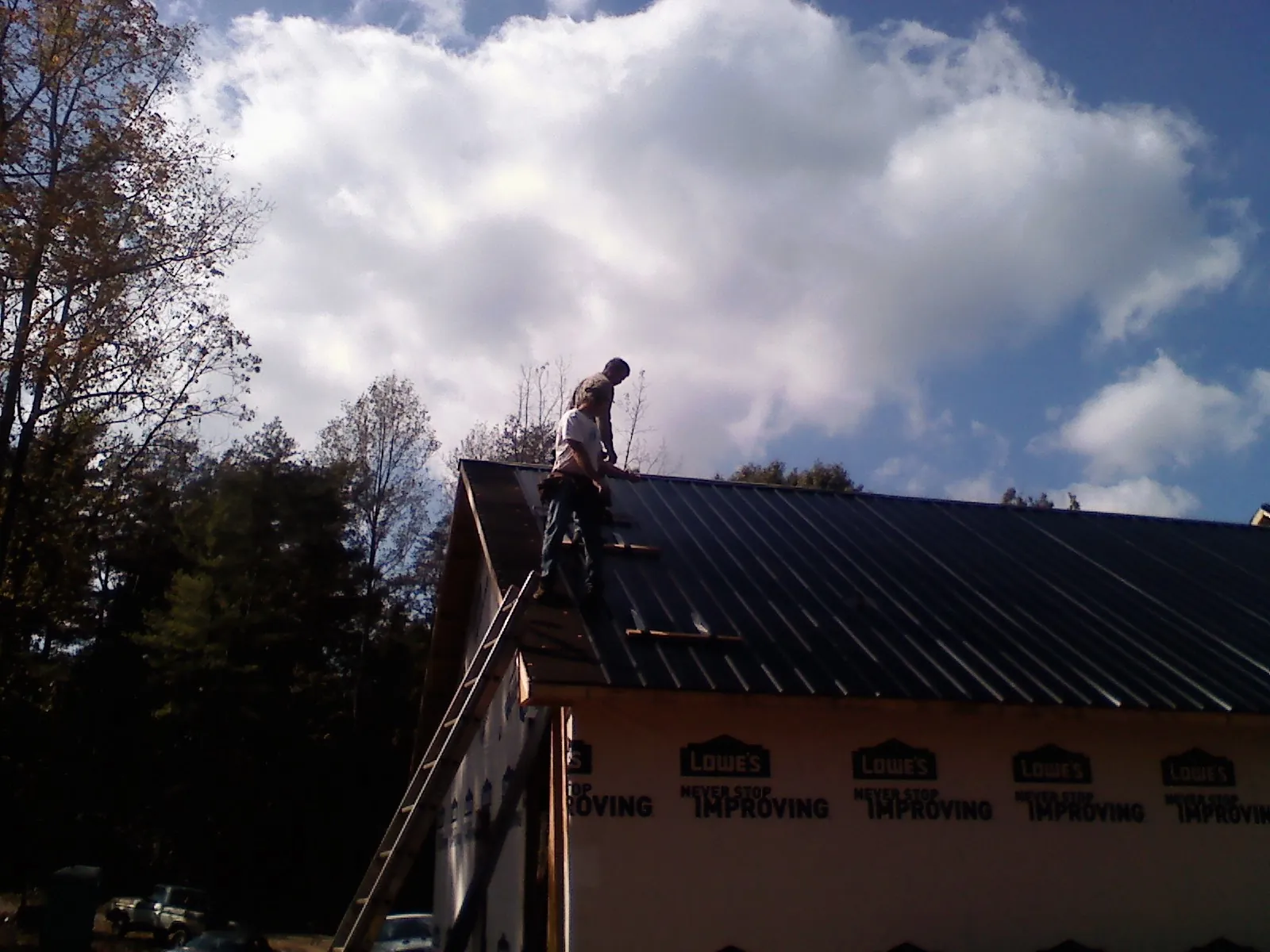Roofer fastening dark metal panels high against a cloudy sky, from a Roof Inspection job in Caldwell