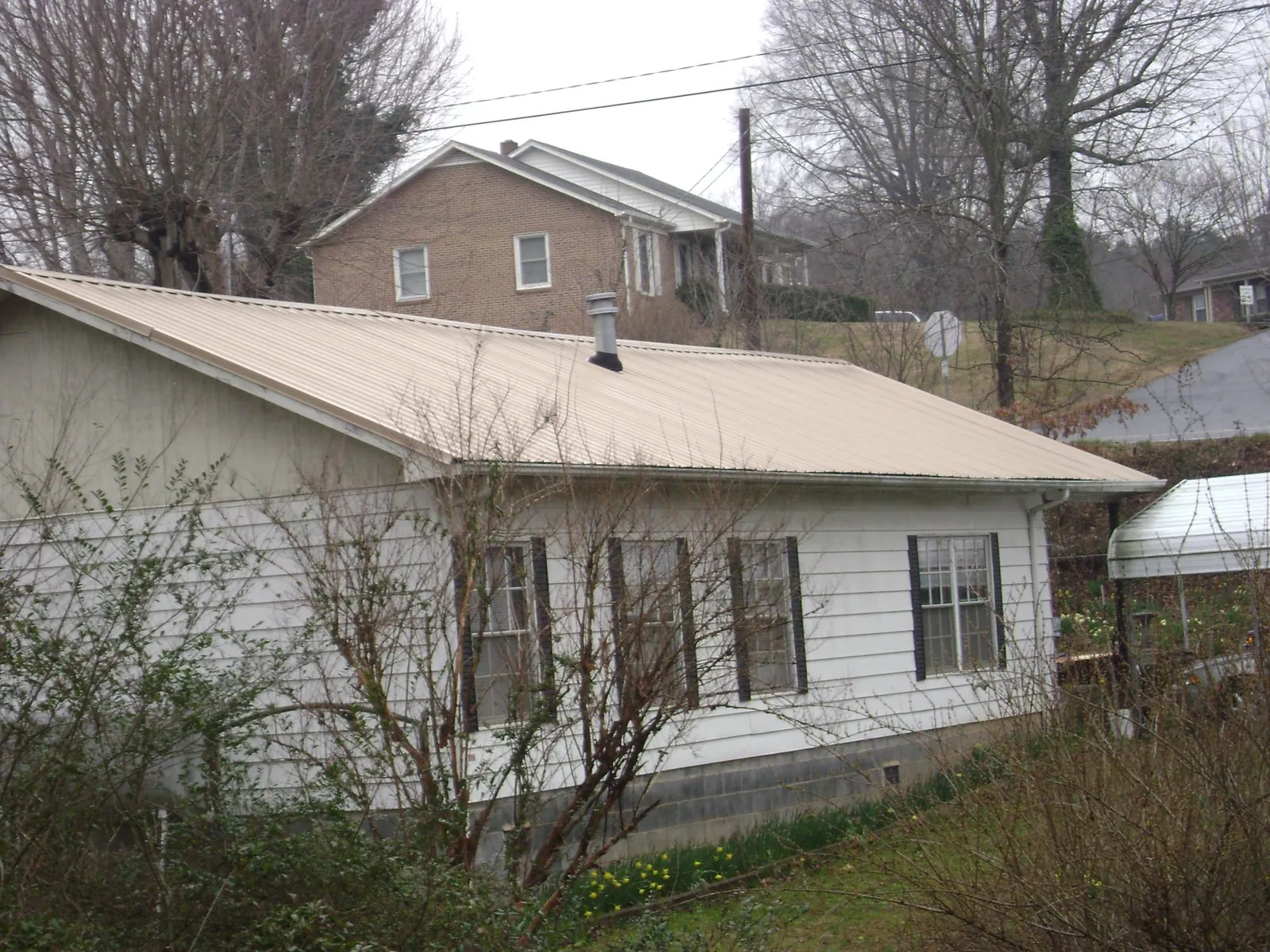 Tan metal roof on a white sided house set into a hillside — Commercial Roofing by Roofing Brothers in Caldwell